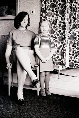 Seated woman in a simple dress and patterned tights holds a pose with a young child in a striped dress and matching tights. I...