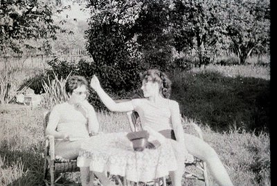 Two young people relax in wicker chairs, casually posed on a grassy lawn with lush foliage in the background. The individual ...