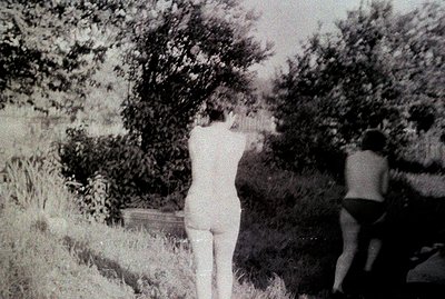 Two figures, appearing nude, are positioned in a dense, overgrown garden setting. The foliage obscures the surroundings, crea...