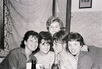 A group of four women, smiling and closely positioned, appear in a domestic setting. They are wearing striped tops and casual...