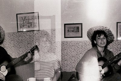 A group gathers for an informal musical gathering in a room featuring textured walls and framed landscapes. A person with a s...