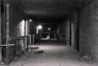A long, dimly lit brick corridor or tunnel. Construction scaffolding and lumber are present, suggesting ongoing or recent wor...