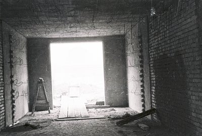 An unfinished brick interior reveals an exterior view through a doorway, suggesting construction or renovation. A wooden plan...