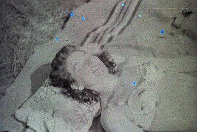 A black and white photo shows a young woman lying prone with her head turned to the side. She wears a dress with delicate det...