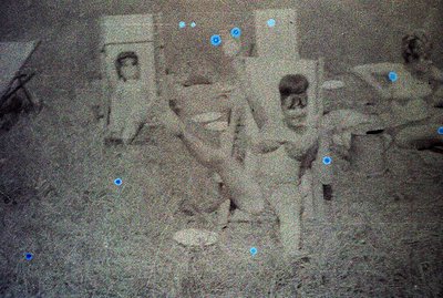 A faded, grainy photograph shows three children in what appears to be a rural or overgrown outdoor setting. One child stands ...