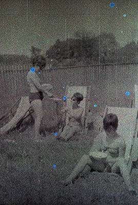 Vintage monochrome photo shows three children near a wooden fence, seemingly engaged in playful activity. One child holds a s...