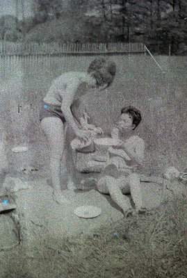 Three children play outdoors; two kneel and one stands, appearing to engage with something on the ground, possibly toys or st...