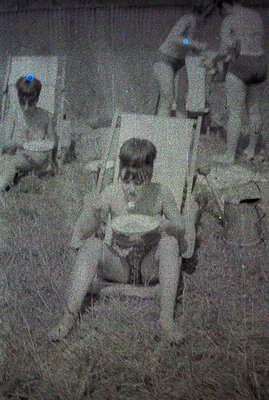 A grainy black and white photograph depicts two young boys seated in folding chairs outdoors. One boy sits facing the camera,...