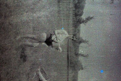 A grainy black-and-white image shows a person in a sharp suit holding a briefcase, ascending an escalator. The escalator's mo...