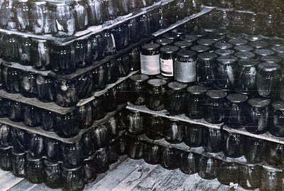 Massive shelving unit densely packed with glass jars, possibly preserves or canning goods. Black and white photo suggests a p...