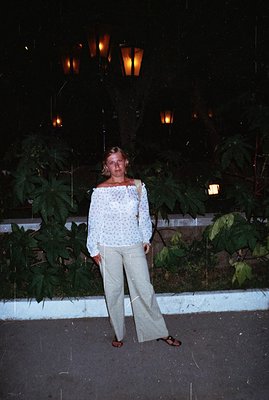 A woman stands outdoors at night, wearing a patterned off-the-shoulder top and wide-leg pants. A vintage aesthetic suggests a...
