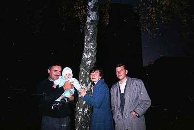 A family portrait, likely a candid snapshot, featuring a man holding a baby, a woman in a blue coat, and a young man, posed n...