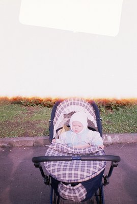 A baby sleeps peacefully in a vintage stroller, wrapped in a plaid blanket and a white bonnet. The photo, likely taken in the...
