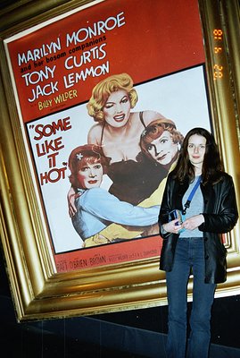 A woman poses in front of a vintage "Some Like It Hot" movie poster featuring Marilyn Monroe, Tony Curtis, and Jack Lemmon. T...
