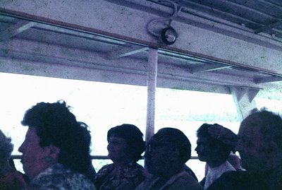 Four individuals are seen through a window, likely on public transportation. The image exhibits a grainy quality characterist...