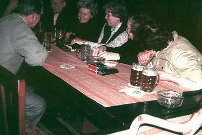 A group of four people gathered around a table laden with drinks. Likely a casual gathering, evidenced by the relaxed posture...