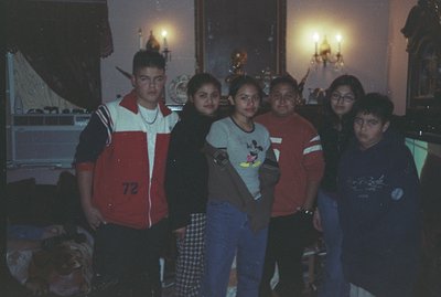 Group portrait of five young people in a richly decorated room. Features include a patterned rug, ornate wallpaper, and lit c...