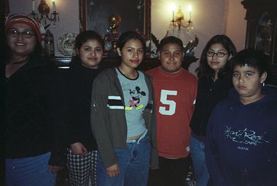 Group portrait of six young people, likely family members, standing indoors. Visible background details include a chandelier,...
