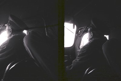 A man in a dark coat and hat sits facing away from the camera, viewed from behind. The scene is brightly lit with light emana...