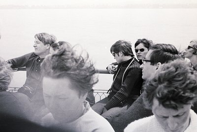 Group of young men, likely tourists, are seated on a boat deck, gazing towards the horizon. Dark, casual clothing and hairsty...
