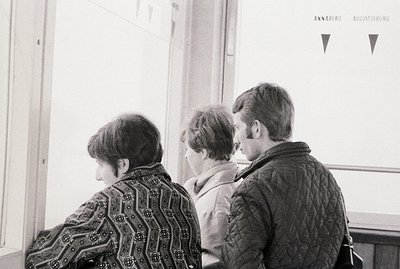 Three figures viewed from behind, likely on a public transportation vehicle; the older woman in patterned jacket, followed by...