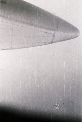 A grayscale, high-angle view focusing on the wing of an aircraft, partially visible. The image exhibits significant dust and ...