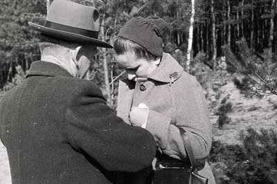 A man in a hat and a woman in a coat appear to share a poignant moment outdoors. The woman holds a tissue to her face, seemin...