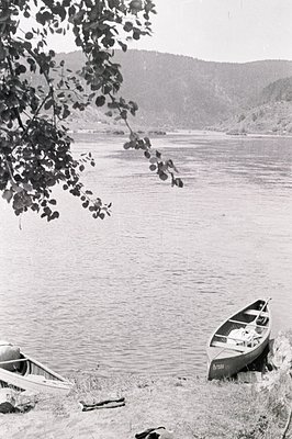A serene lakescape featuring two small rowboats resting on a grassy shoreline. Gentle slopes rise into the distance, creating...