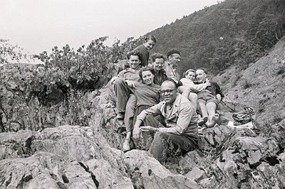Six individuals pose on a rocky hillside, appearing to be enjoying a leisure outing. The group's attire – casual shirts, trou...