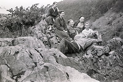 Five individuals casually posed on a rocky hillside; several are seated or reclined on the stone. Clothing suggests a mid-cen...