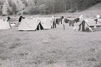 A sprawling campsite is nestled within a valley, showcasing several tents and a clothesline laden with drying garments. Lush,...