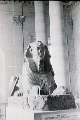 Monochrome photo of an ancient Egyptian sphinx statue displayed indoors. The sphinx features a pharaoh's headdress and a lion...