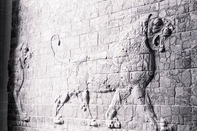 Detailed relief carving depicting a lion with a bull's head (lamassu) embedded within a stone wall. The figure displays a com...