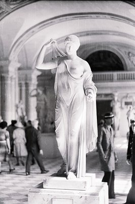 Dramatic black & white photo: a marble statue of a draped female figure stands within an ornate, classical-style interior. Vi...