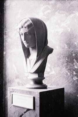 Classical bust of a woman draped in a flowing veil, displayed on a stone pedestal. The marble sculpture exhibits detailed fac...