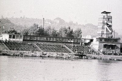 A view of a large, tiered seating structure and a distinctive multi-story observation tower alongside a waterway. Spectators ...