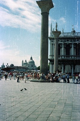 A wide-angle view of St. Mark's Square in Venice, Italy, featuring a massive Corinthian column and the Basilica di San Marco ...