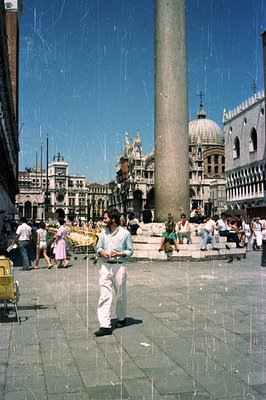 Vintage color photograph of Venice's Piazza San Marco, c. 1970s. A man in a short-sleeved shirt and white pants walks toward ...