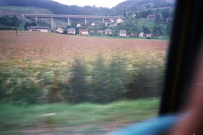 View from within a vehicle, showcasing a rural landscape with a multi-span bridge in the distance. A valley with houses and v...