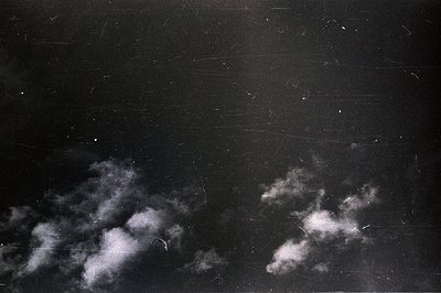 Strikingly textured black and white image depicting clouds at night. Visible scratches and marks across the surface suggest a...