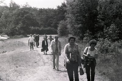 Group of people walk along a rural road, likely in Bulgaria. The image captures casual attire of the 1970s - wide-legged trou...