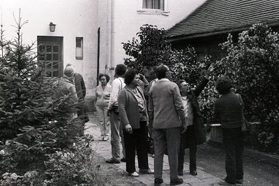 A group of formally-dressed people walk along a stone path toward a building facade. Architectural details show a mix of bric...