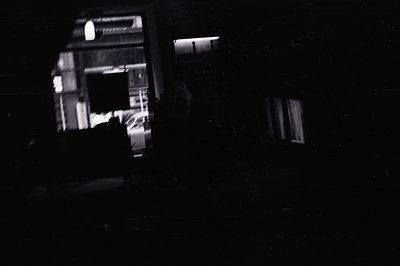 A black and white photograph depicts a car within a garage. Light from the garage spills outward, illuminating a partial view...