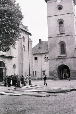 A gray, monochrome image showcases a medieval courtyard with a prominent stone tower featuring arched windows and a clock fac...