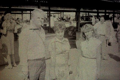 Four individuals stand in a crowded, seemingly public space with architectural detailing – possibly a transport hub. The grou...