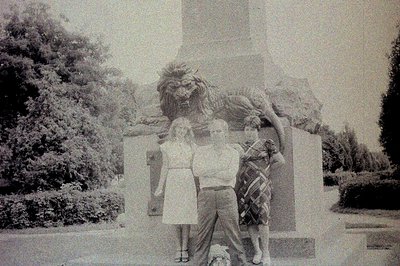 Three young people pose in front of a monumental stone sculpture depicting a lion and female figure – possibly allegorical. A...