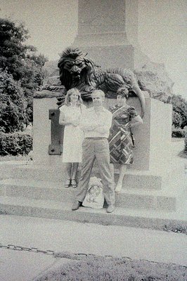 Three people pose before a monumental bronze statue depicting a lion, potentially a symbolic or allegorical representation. T...
