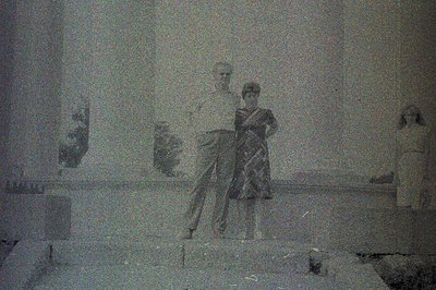 A grainy black and white image depicts three figures on tiered steps. Two adults, a man in a short-sleeved shirt and a woman ...