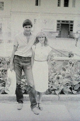 A couple strolls along a paved walkway in front of a stately building featuring arched windows and ornate detailing. The man ...