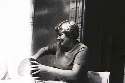 A woman in a textured knit top sits at a table, carefully cradling a ceramic bowl. The scene is brightly lit, creating strong...